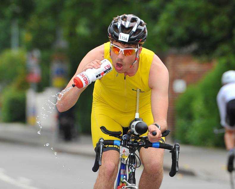 A bicyclist trying to drink from the wrong side of the water bottle. Water is spraying everywhere. 