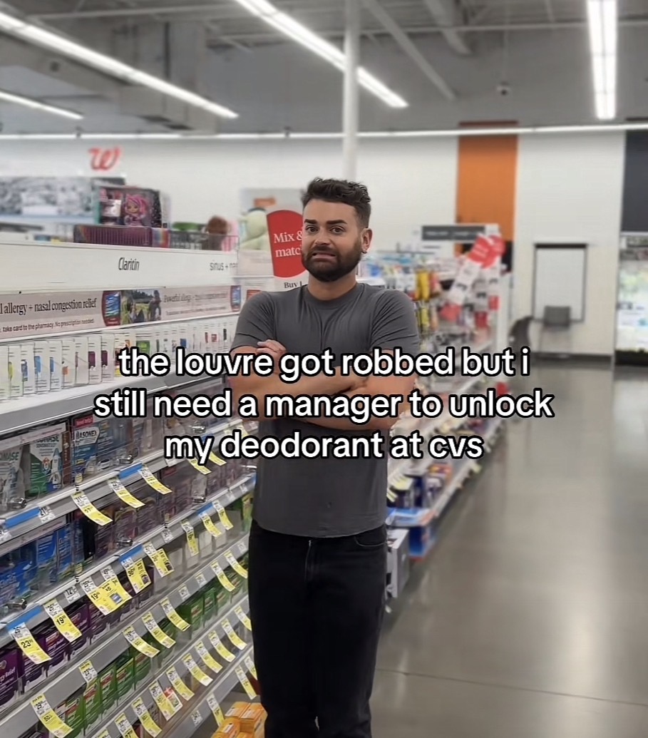 A person standing on a store aisle with their arms crossed with the caption “the louvre got robbed but i still need a manager to unlock my deodorant at CVS”