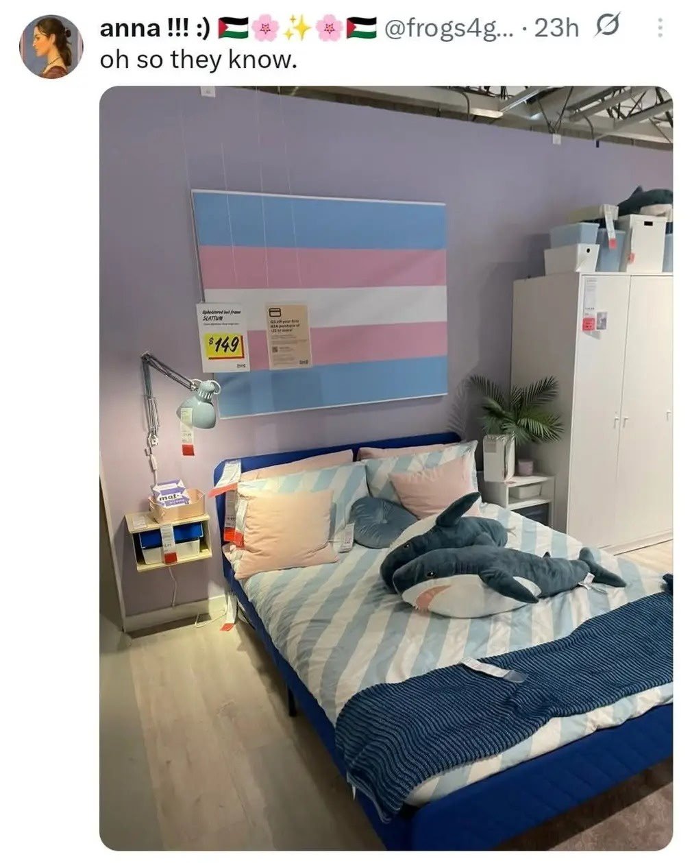An IKEA bedroom set featuring a trans pride flag and blahaj stuffed animal. 
