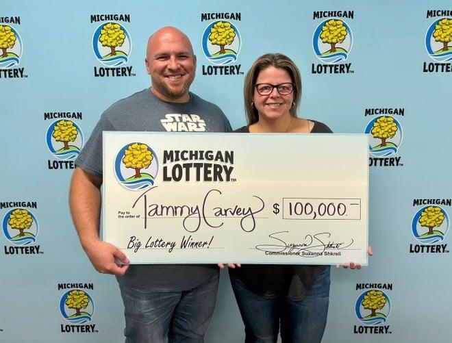 La foto riproduce la vincitrice del biglietto della Lotteria con il marito. Entrambi tengono in mano un maxi assegno deòòa Michigan Lottery di 100 mila dollari