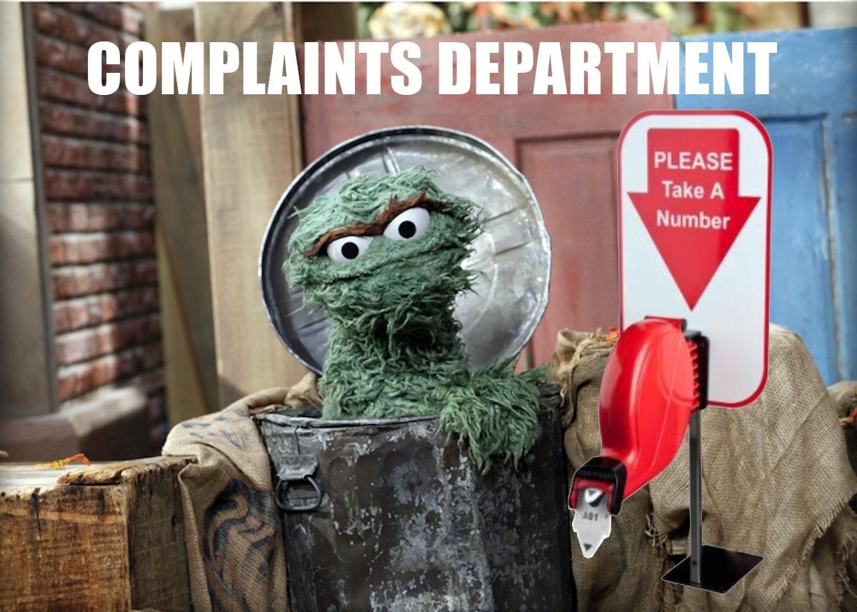 oscar the gouch with a deli ticket machine next to him, the sign reads "PLEASE Take A Number", the top text reads "COMPLAINTS DEPARTMENT"